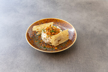 Sophisticated Spanish tapa of Russian salad topped with fried shrimp, chives and accompanied by crispy potato on the sides on a toasted brown plate