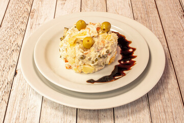 Salad top with mayonnaise, pitted olives, potato, egg and cooked carrot on white restaurant plates