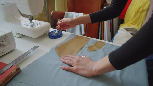 Tilt up shot of professional female dressmaker pinning pattern pieces to fabric while working in sewing studio