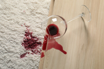 Overturned glass and spilled red wine on white carpet indoors, above view