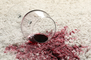 Overturned glass and spilled red wine on white carpet, closeup