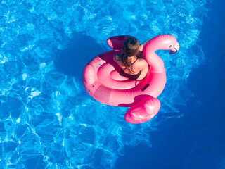 Summer background. Beautiful woman floating on pool flamingo float in pool in hotel. Summer holidays, enjoying summer vacations during quarantine. Aerial drone view