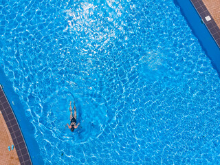 Aerial top view of woman in swimming pool water from above, tropical vacation holiday concept, drone view