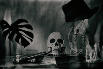 Fototapeta na wymiar still life imitate wet plate photography style focus Skull and snap pearl necklace on old book and a large glass bottle with fedora Gangster and cross necklace 
