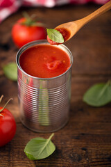 Open tin of tomatoes sauce with whole fresh tomatoes on a rustic wooden table