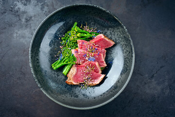 Modern style baby broccoli with fried dry aged sliced beef fillet steak served as top view on a...