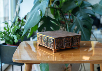 Mid-century modern copper music box on a wooden table with plants in the background