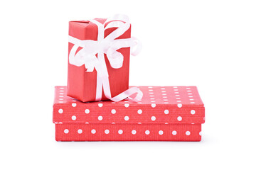 A gift box wrapped in red wrapping paper with white ribbon on top of a red box with polka dots,...