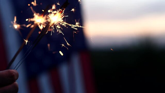 Happy 4th of July Independence Day. Hands holding sparklers celebration with American flag at sunset nature background, soft focus. Concept Independence Day, Memorial, Veterans, Celebrate, Fireworks.