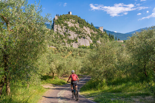 nice and active senior woman riding her electric mountain bike in the Garda lake mountains between blooming the olive groves of Arco close to Riva del Garda and Garda Lake , Landscape