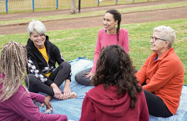 Multi generational women having fun talking and sitting at city park - Multiracial people enjoy day...