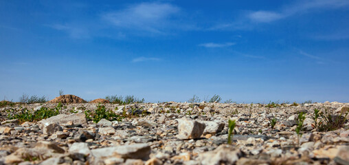 Fototapeta na wymiar Panorama of desert rocky land and blue sky. Stony soil with sparse vegetation. Bottom view. Industrial dumps.
