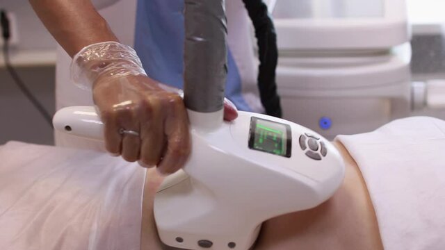 Hardware anti-cellulite massage. RF lifting procedure. The beautician guides the device along the client's belly. Ultrasound cavitation body contouring treatment. Anti-fat therapy.