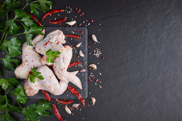 Raw chicken wings with ingredients for cooking. Raw meat. Chicken wings lie on a wooden board with vegetables and spices on a black background. background image, copy space text.