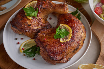 Grilled chicken legs in barbecue sauce and roasted vegetables with tomatoes, pepper seeds, salt, lemon in the white plate on light color  stone table. Top view, copy space. Tasty snack . Flat lay.