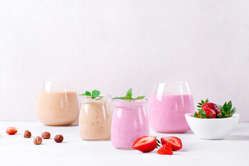 Pink and yellow smoothies topped with mint in glass jars on the white table. Healthy drink and kids food