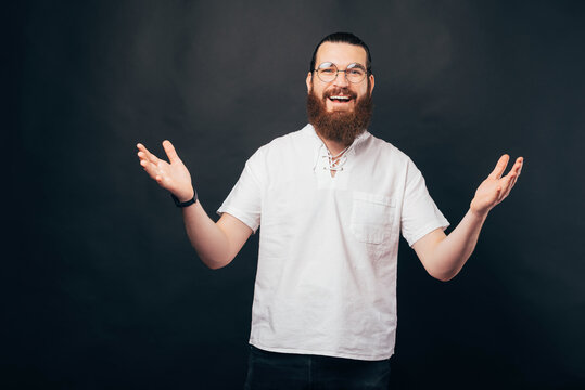 Photo of young bearded hipster man wearing round glasses and making welcome gesture