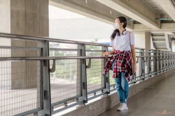 An Asian girl wearing a mask walks dejectedly on a footbridge.