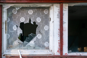 Small broken window with red frame and window shades torn apart. Detail of an old abandoned house,...