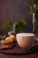 coffee with milk foam in a glass mug on a wooden table next to a bouquet of wildflowers and cookies