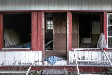 Old abandoned wooden house falling apart. Broken windows, scattered glass, white walls, red doors...