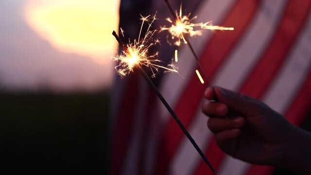 Happy 4th of July Independence Day. Hands holding sparklers celebration with American flag at sunset nature background, soft focus. Concept Independence Day, Memorial, Veterans, Celebrate, Fireworks.
