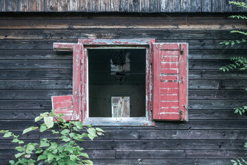 Detail of a broken window of old abandoned wooden house. Red window shutters are open and falling...