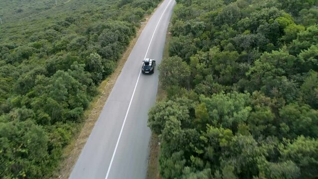 Aerial shot following a car driving on a mountain road through the woods