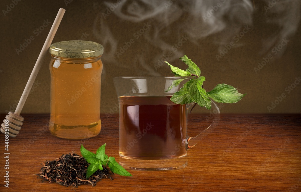 Wall mural aromatic herbal hot tea in glass teacup on a wooden desk.