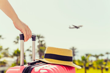 Woman with pink suitcase and beach hat standing on passengers ladder and getting out of airplane...