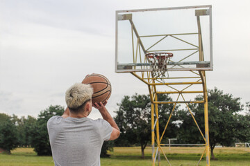 Rear shot of a young man preparing to shoot the ball, on an abandoned basketball court.