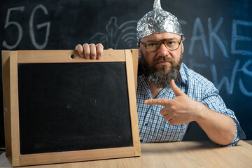 A strange bearded conspiracy theorist in a protective aluminum foil hat and glasses sits at a table...