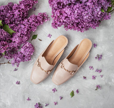 Beige leather mules top view on the gray background with flowers