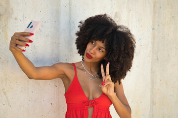 Beautiful young african american woman with afro hair with coral top and white skirt taking a selfie.