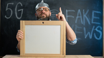 stupid conspiracy theory guy in a foil hat holds a blackboard with space for text. A bearded...