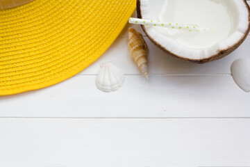 Top view of yellow summer hat and coconut water on white wooden table with copy space