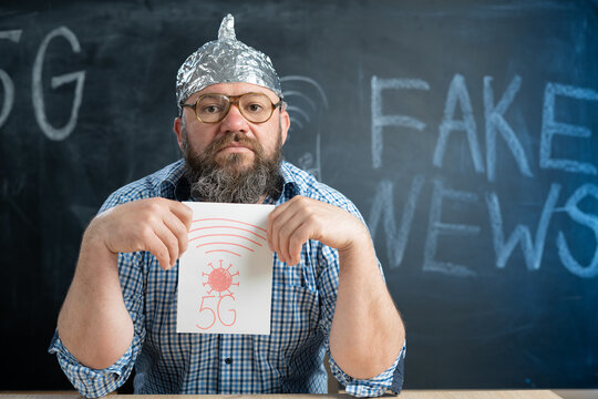Conspiracy and a man sits at the blackboard and holds a sign 5g in his hands. Chalk board in the background with place for text. Conspiracy theorist and fake news. conspiracy theory.