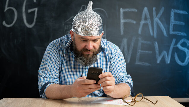 portrait of a crazy conspiracy theorist with a mobile phone in his hands and a protective cap made of foil is of electric waves and radiation. Conspiracy theory and the Internet user.