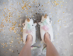 Feet with Unicorn slippers on grey background with glitter stars top view