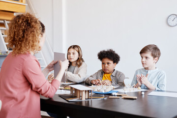 Group of children making cardboard models while enjoying art and craft class in school with female teacher, copy space