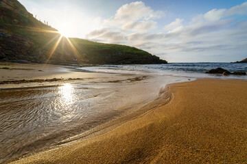 Sunset on the golden sand beach with small pools of water reflecting the sun.