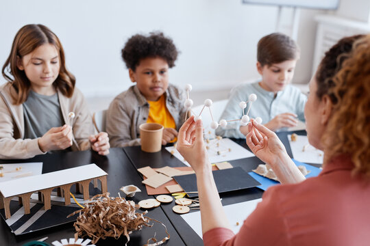 Back view at female teacher demonstrating wooden models to group of kids during art and craft class in school - Powered by Adobe
