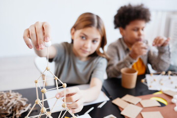 Portrait of teen girl making wooden models during art and craft class in school, focus on foreground