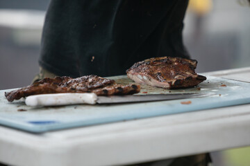 A man cutting up barbeque ribs from the smoker grill on cutting board with gloves on and a large knife.