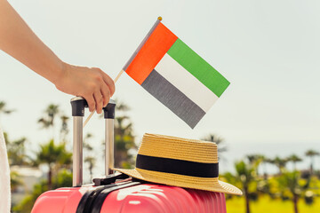 Woman with pink suitcase and United Arab Emirates flag standing on passengers ladder and getting out of airplane opposite sea coastline with palm trees.