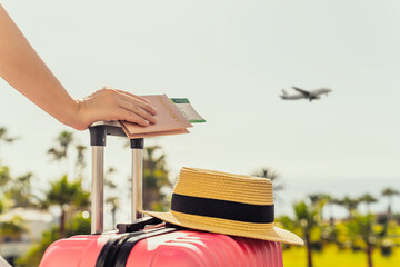 Woman with pink suitcase and passport with boarding pass standing on passengers ladder of airplane...