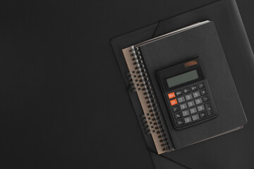 Calculator, notebook on black leather background.