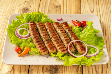 Chevapchichi, a meat appetizer on a wooden table. Lettuce leaves and hot pepper complement the meat dish. Lula-Kebab. Selective focus.
