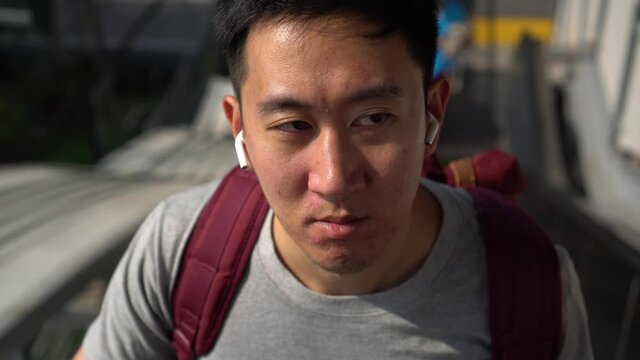Close up of young man listening to music with wireless earpods while commuting by train at station. Asian guy enjoying music on the go.