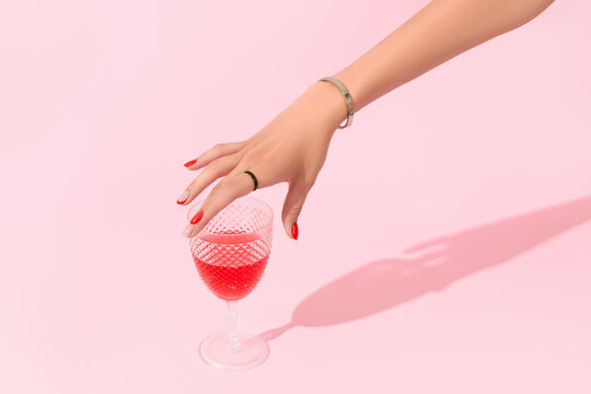 Womans hand holding glass on pink background. Manicure design trends